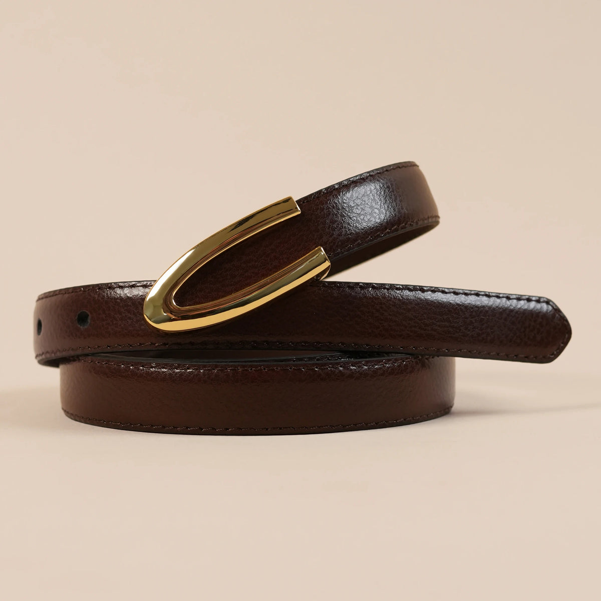 Close-up of the Darci belt's polished gold U buckle on brown leather