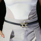 Black Scarlett belt with gold buckle worn over grey trousers