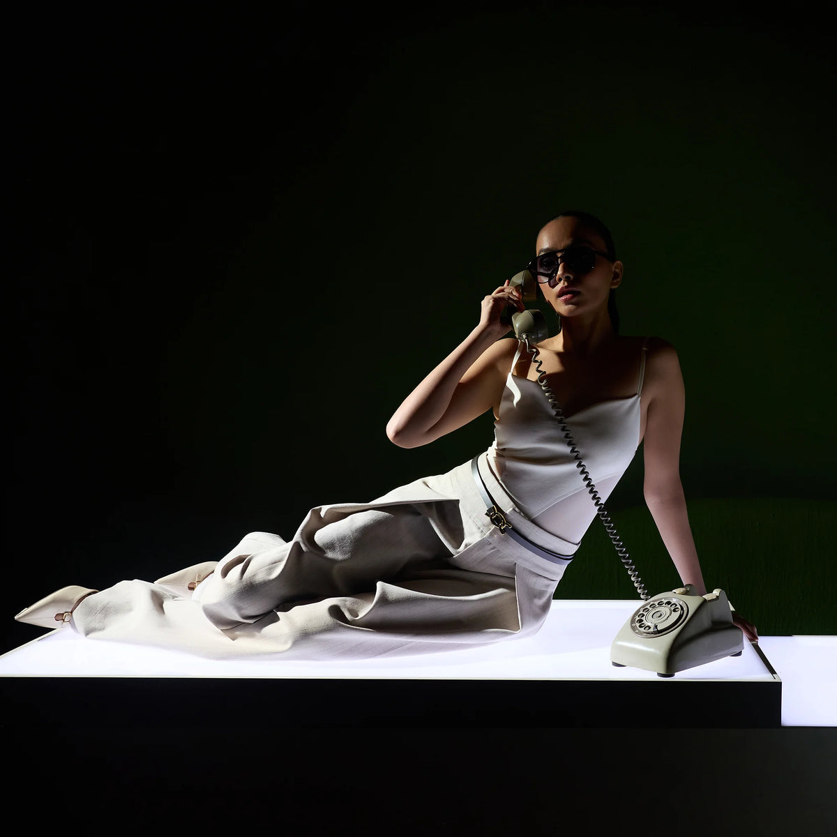 Woman reclining on a white plinth with a phone, wearing the black Scarlett belt