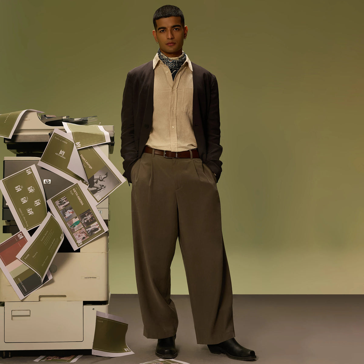 Man in a brown cardigan and olive trousers wearing the Savora belt brown side out by a photocopier